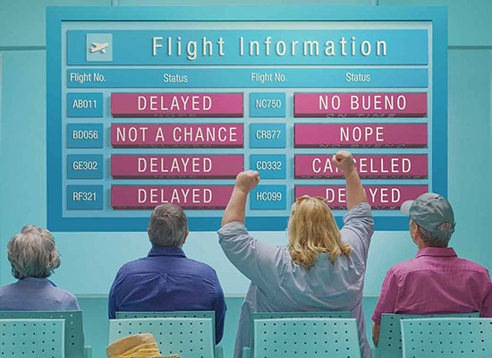 Woman cheers in airport waiting room in front of a display where all flights read delayed or cancelled