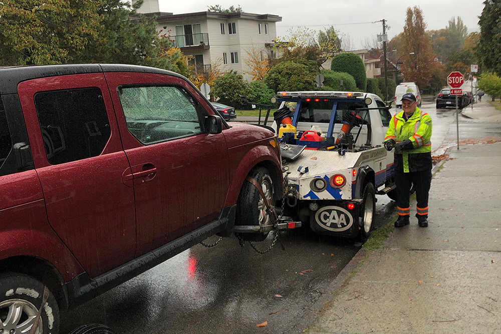 Red car being loaded onto a BCAA tow truck on a rainy day