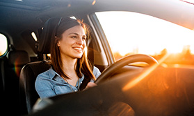 Woman sitting in drivers seat of car at sunset