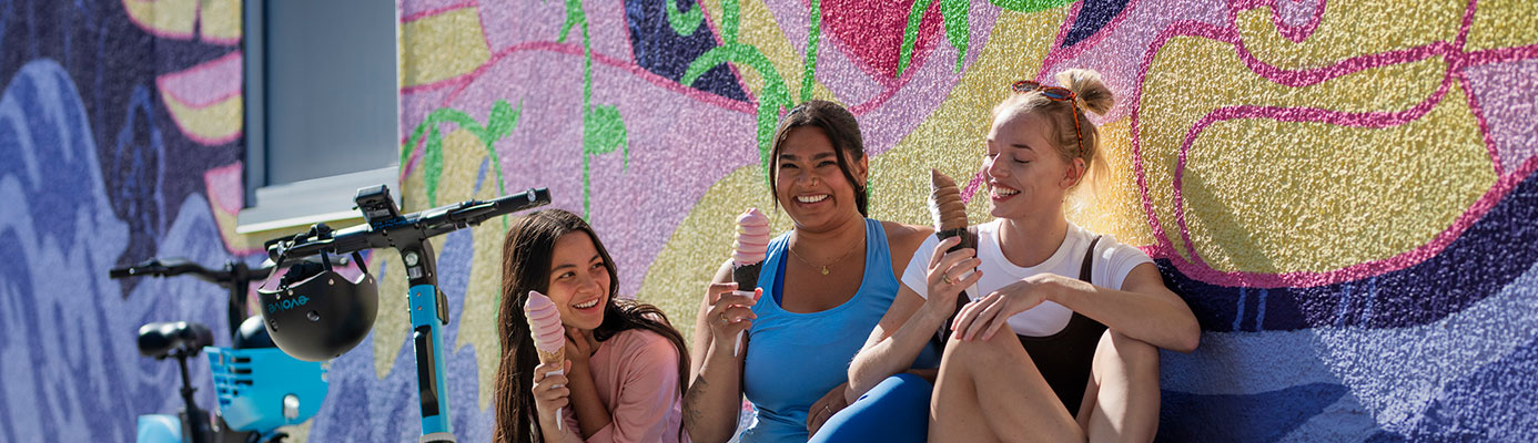 Girls sitting near a mural wall and enjoying ice cream on a warm summer day