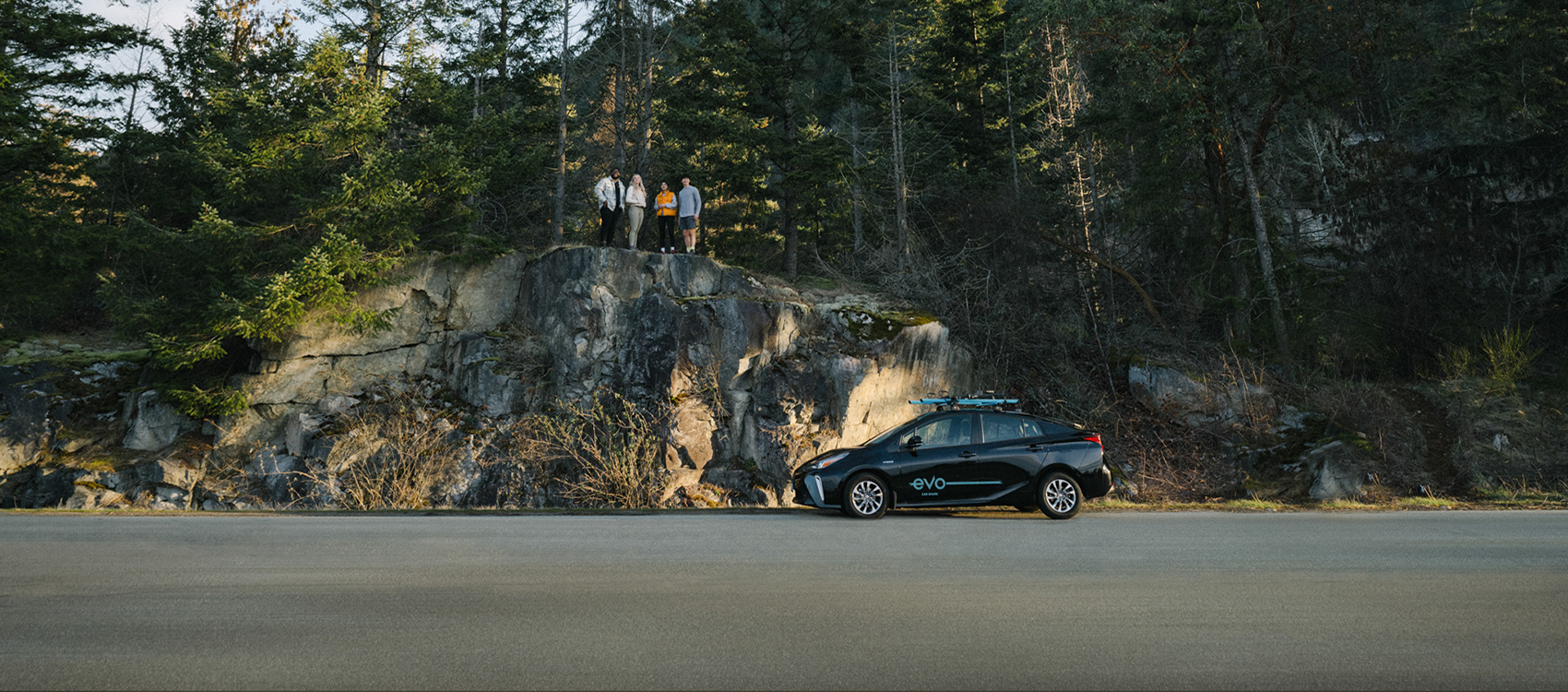 Four friends standing on a rocky outcrop over an Evo vehicle