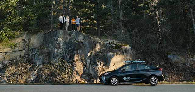 Group of friends standing on rocky landscape behind an Evo car