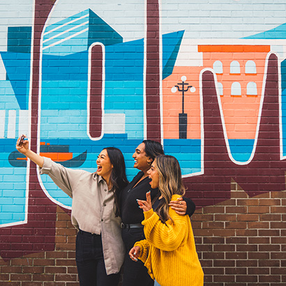 Friends posing for a selfie in front of a blue and orange mural