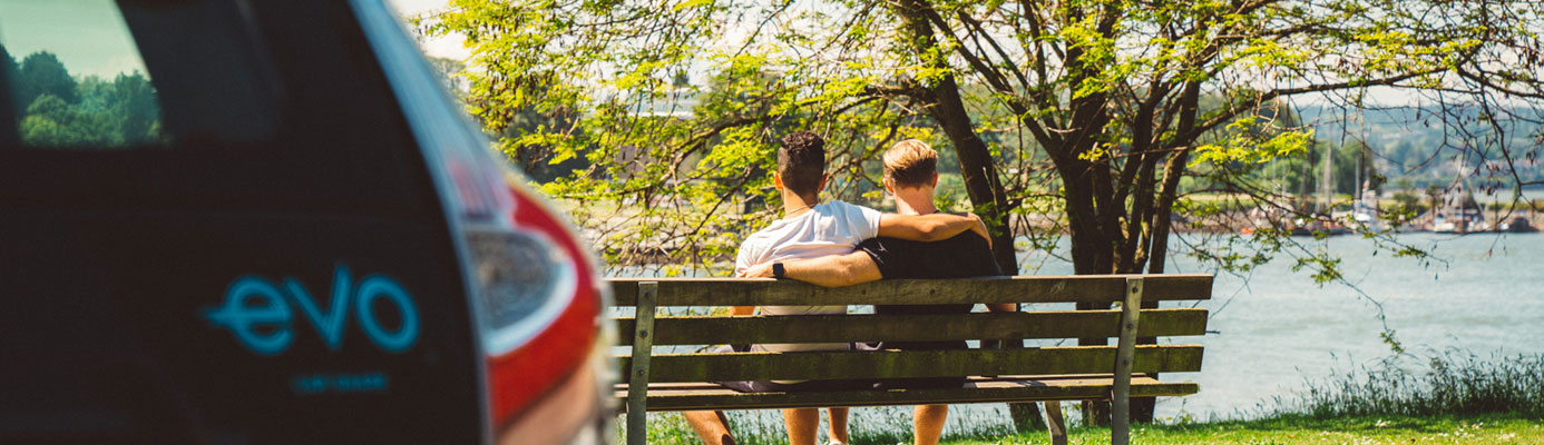 couple sitting on park bench next to an evo car