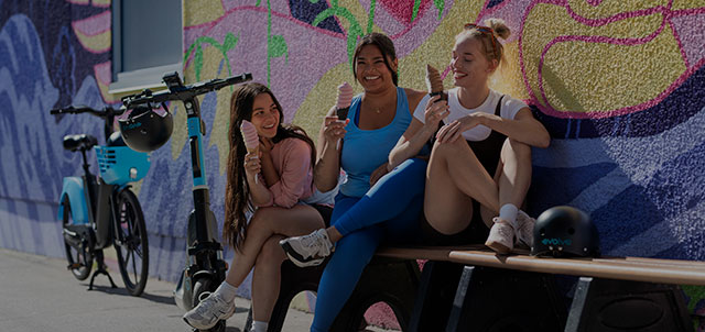 Friends enjoying ice cream beside parked Evolve e-bikes and e-scooter