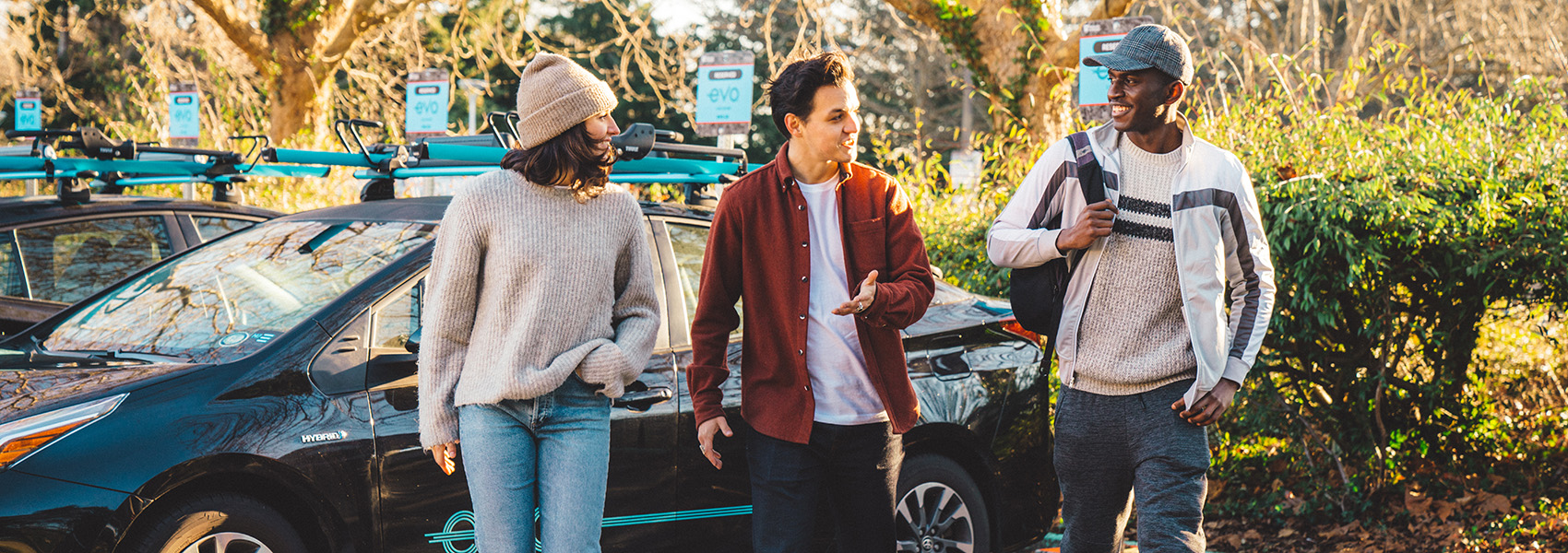 Three friends walking away from a parked Evo with trees and shrubs behind
