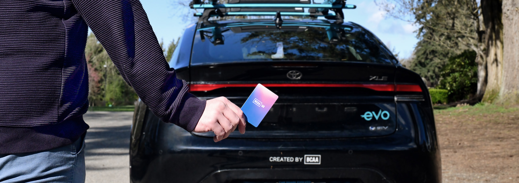 Person holding BCAA GO Membership card in front of a parked Evo vehicle.